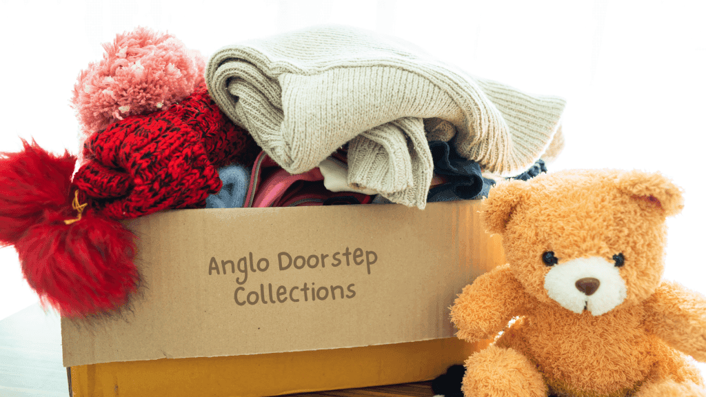 Cardboard box with teddy bear, clothes and hats inside. 